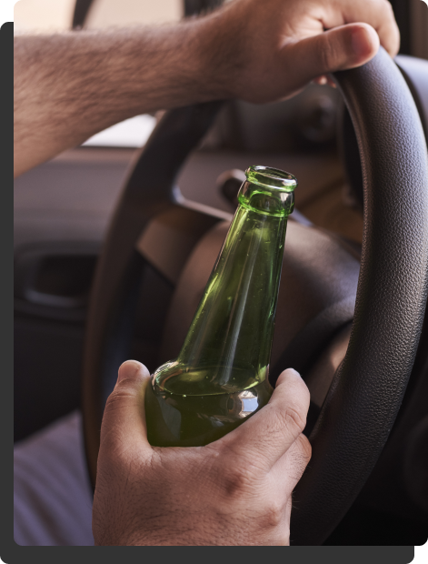 A man holding the car steering wheel and a bottle of alcohol